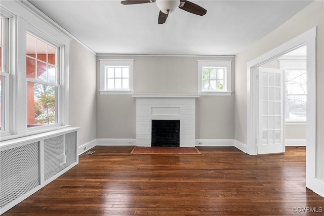 unfurnished living room featuring a brick fireplace, dark hardwood / wood-style floors, radiator heating unit, and ceiling fan