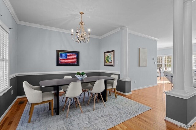 dining area featuring wood-type flooring, ornamental molding, a chandelier, and ornate columns