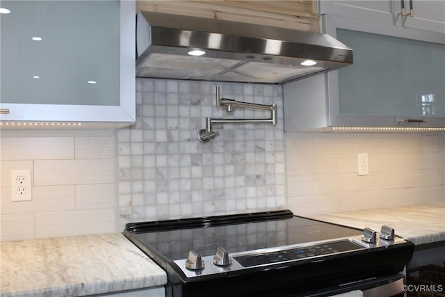 kitchen with extractor fan, backsplash, and light stone countertops