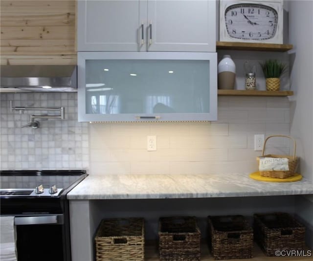 kitchen featuring light stone counters, white cabinets, backsplash, and black / electric stove