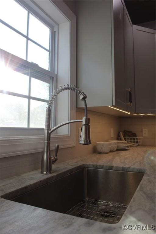 interior details featuring sink, tasteful backsplash, and light stone countertops