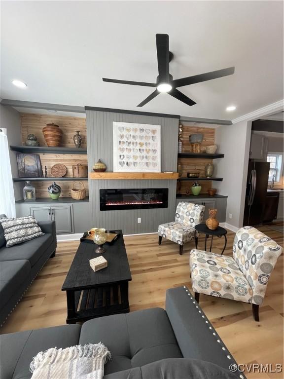 living room with crown molding, a large fireplace, built in shelves, and light wood-type flooring