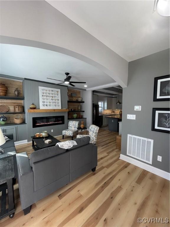 living room featuring ceiling fan, light wood-type flooring, and a fireplace