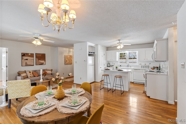 dining space with ceiling fan with notable chandelier, a textured ceiling, light hardwood / wood-style flooring, and sink