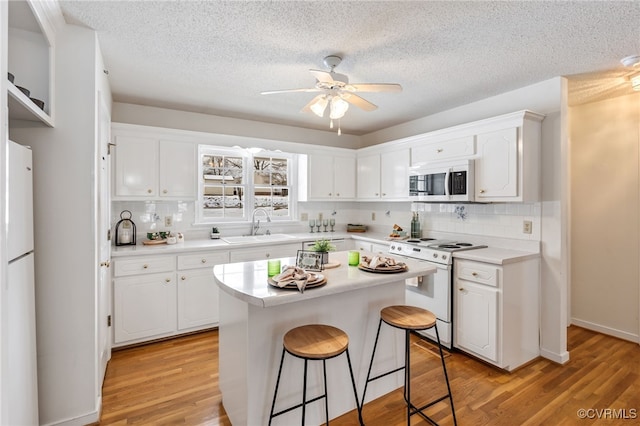 kitchen featuring a breakfast bar, white appliances, sink, a center island, and white cabinetry