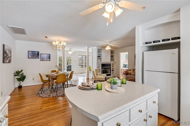 kitchen with a textured ceiling, white refrigerator, built in features, a center island, and white cabinetry