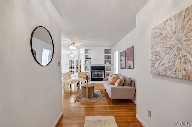 living room with ceiling fan, built in features, a textured ceiling, and light hardwood / wood-style flooring