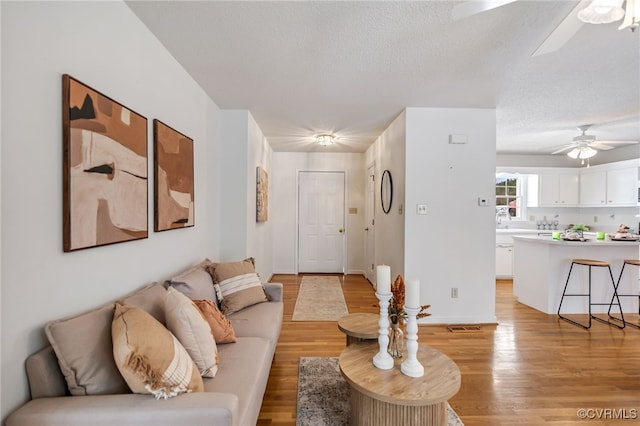 living room with ceiling fan, light hardwood / wood-style floors, and a textured ceiling