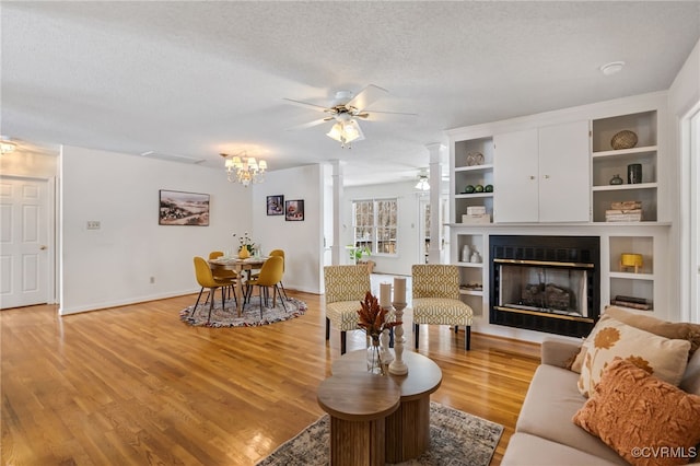 living room with ceiling fan with notable chandelier, light wood-type flooring, and a textured ceiling