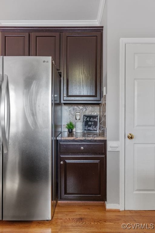 kitchen featuring stainless steel fridge, light hardwood / wood-style floors, backsplash, ornamental molding, and dark brown cabinets