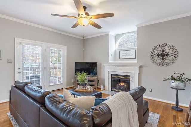 living room featuring crown molding, a fireplace, ceiling fan, and light hardwood / wood-style flooring