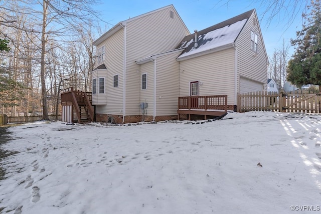 snow covered back of property featuring a garage and a wooden deck