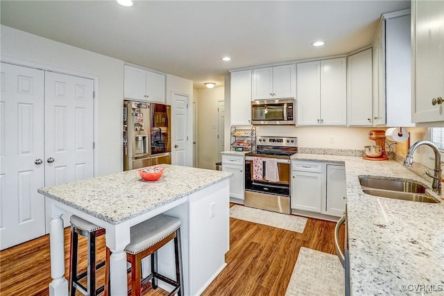 kitchen with white cabinetry, stainless steel appliances, sink, light stone counters, and a breakfast bar area