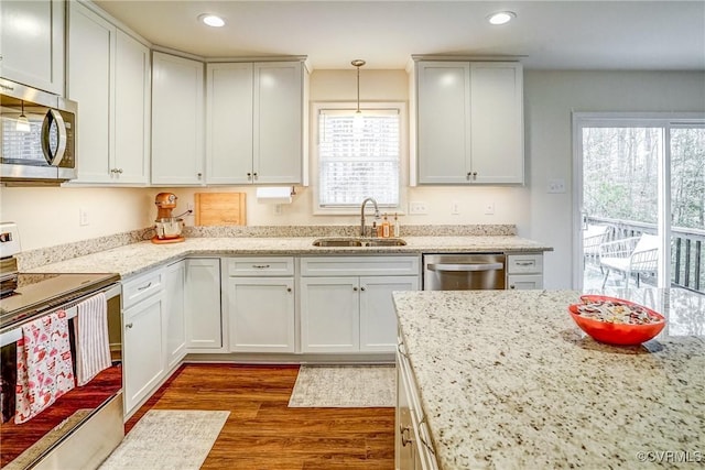 kitchen with sink, stainless steel appliances, white cabinetry, and decorative light fixtures