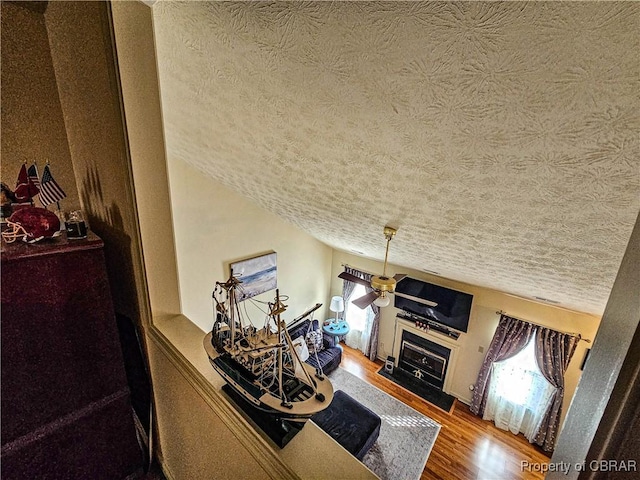 living area featuring wood finished floors, a fireplace with flush hearth, a ceiling fan, and a healthy amount of sunlight