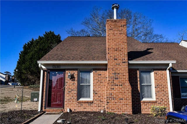 view of front of property with roof with shingles, brick siding, and a chimney