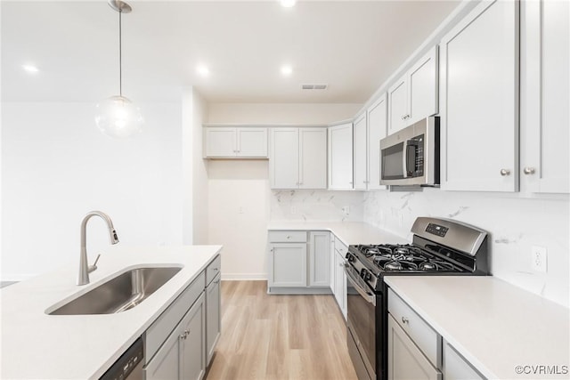 kitchen featuring hanging light fixtures, stainless steel appliances, light wood-type flooring, backsplash, and sink