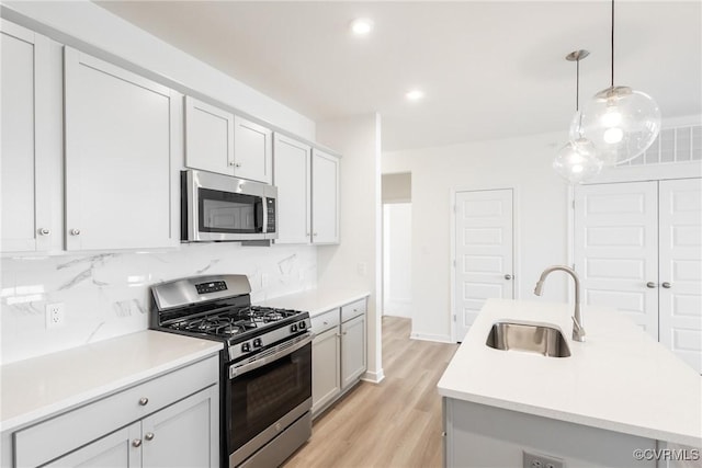 kitchen with appliances with stainless steel finishes, hanging light fixtures, an island with sink, decorative backsplash, and sink