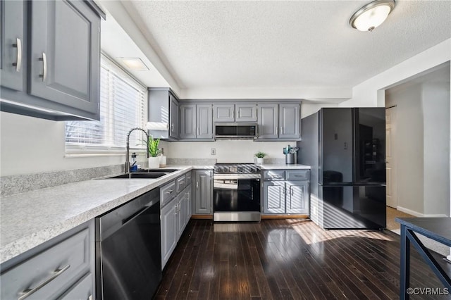 kitchen featuring stainless steel appliances, sink, a textured ceiling, gray cabinetry, and dark wood-type flooring