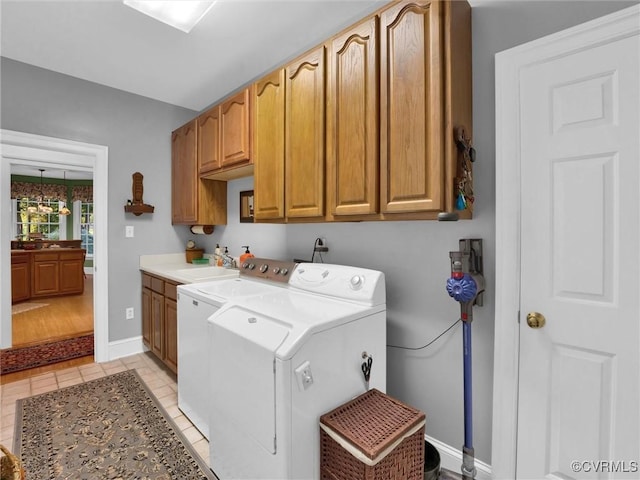 clothes washing area with washer and dryer, sink, light tile patterned floors, and cabinets