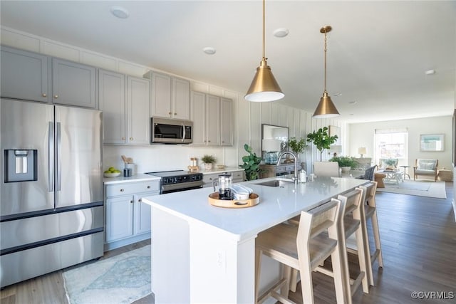 kitchen featuring a kitchen breakfast bar, a kitchen island with sink, appliances with stainless steel finishes, hanging light fixtures, and sink