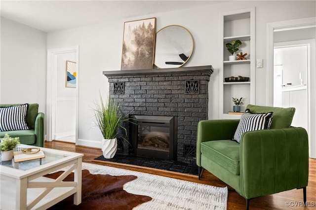 sitting room with a brick fireplace, built in shelves, and hardwood / wood-style flooring