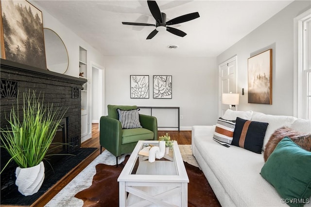 living room with a fireplace, ceiling fan, built in features, and dark hardwood / wood-style floors