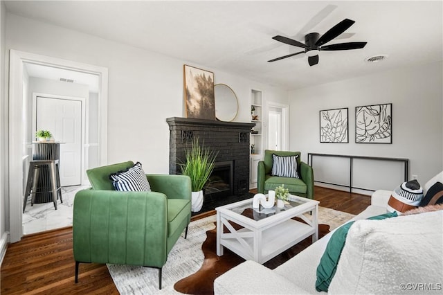 living room with wood-type flooring, a brick fireplace, and ceiling fan