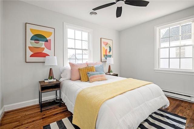 bedroom with ceiling fan, dark hardwood / wood-style flooring, and a baseboard heating unit