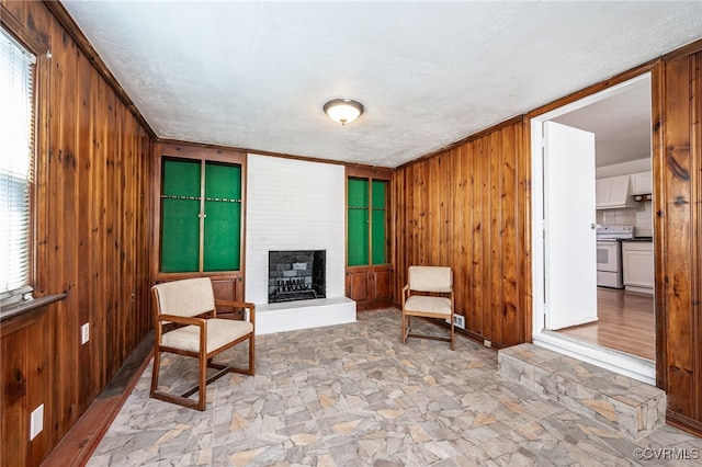 sitting room with a brick fireplace, a textured ceiling, and wood walls