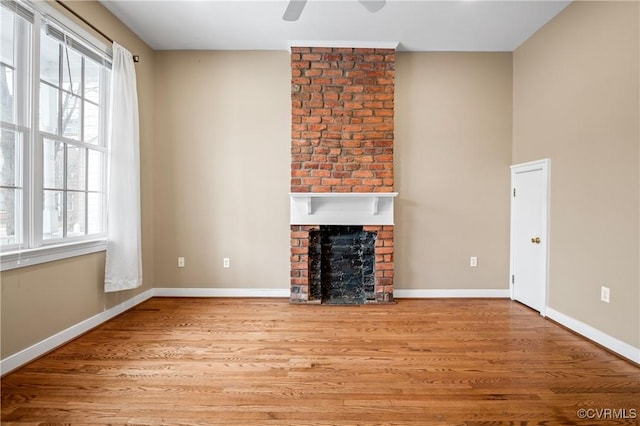 unfurnished living room featuring ceiling fan, a wealth of natural light, a fireplace, and light hardwood / wood-style flooring