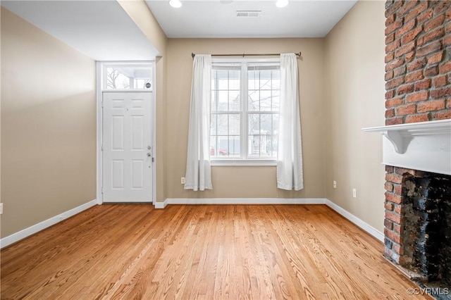 foyer entrance with a brick fireplace and light wood-type flooring