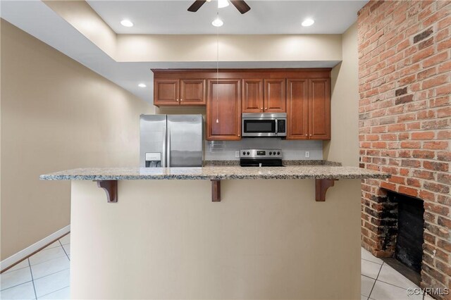 kitchen with appliances with stainless steel finishes, a center island, light tile patterned flooring, light stone counters, and a breakfast bar