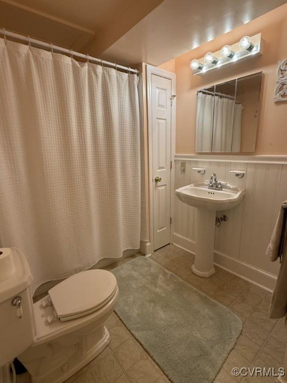 full bathroom featuring wainscoting, toilet, curtained shower, tile patterned flooring, and a sink