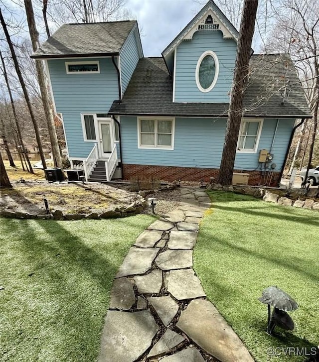 back of property featuring a shingled roof, entry steps, and a lawn