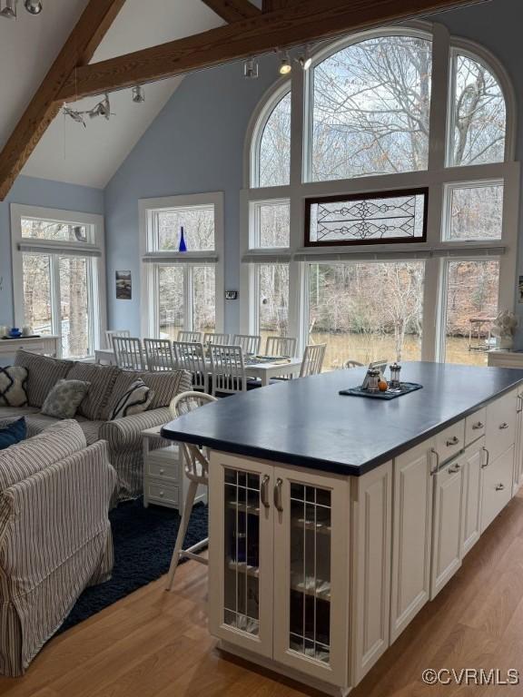 kitchen featuring light wood-style flooring, glass insert cabinets, white cabinetry, high vaulted ceiling, and beamed ceiling