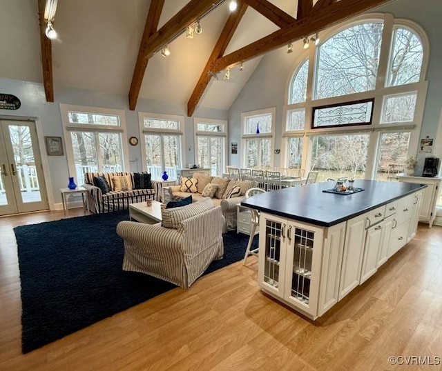 living room featuring beamed ceiling, rail lighting, french doors, light wood-style floors, and high vaulted ceiling