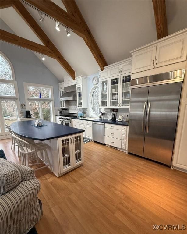 kitchen with dark countertops, light wood-style floors, glass insert cabinets, and high end appliances