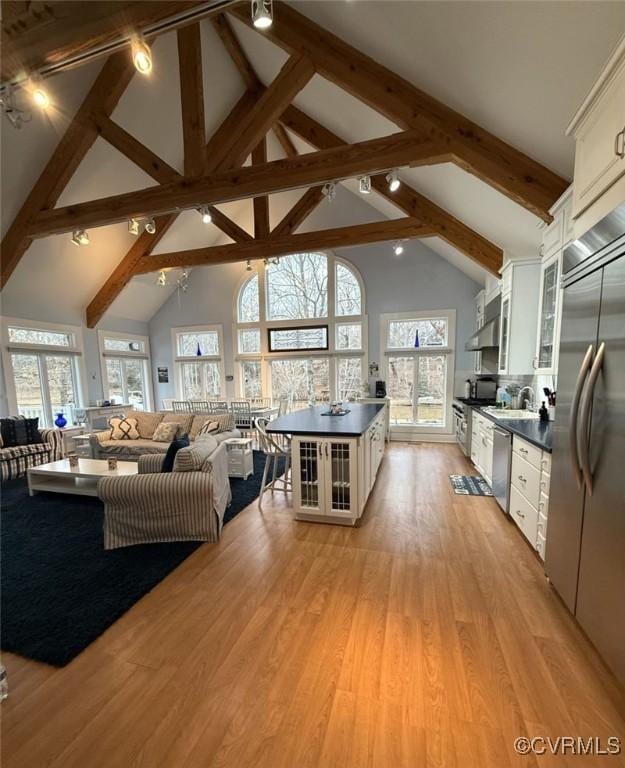 kitchen featuring open floor plan, stainless steel appliances, dark countertops, and light wood-style floors