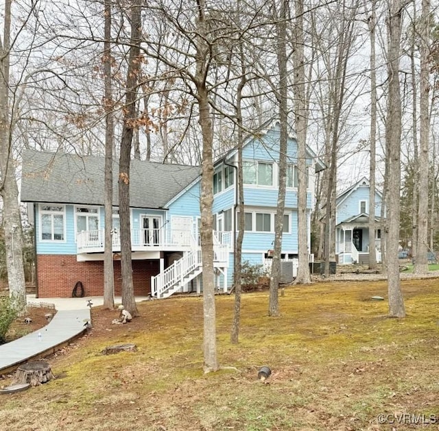 view of front of property with brick siding, roof with shingles, a front yard, a wooden deck, and stairs