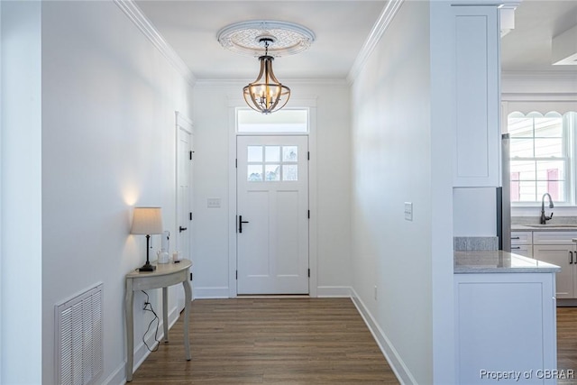 entryway with sink, dark wood-type flooring, crown molding, and a chandelier