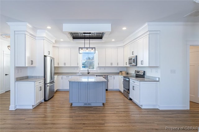 kitchen with pendant lighting, stainless steel appliances, a kitchen island, white cabinetry, and sink