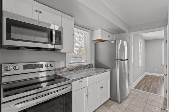 kitchen featuring light tile patterned floors, white cabinets, light stone counters, and appliances with stainless steel finishes