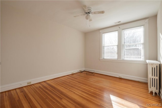 empty room with ceiling fan, light hardwood / wood-style floors, and radiator heating unit