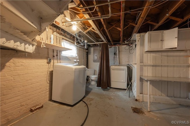 basement with brick wall and washing machine and clothes dryer