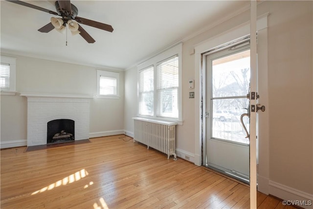 unfurnished living room featuring radiator, ceiling fan, ornamental molding, a brick fireplace, and light hardwood / wood-style flooring