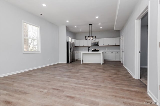 kitchen featuring white cabinetry, hanging light fixtures, light hardwood / wood-style flooring, a kitchen island, and stainless steel appliances