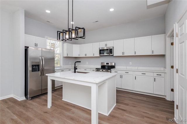 kitchen with sink, white cabinetry, appliances with stainless steel finishes, light stone countertops, and a kitchen island with sink