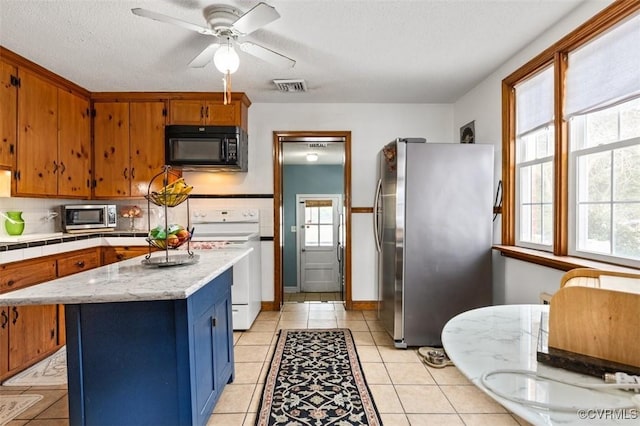 kitchen with a textured ceiling, a center island, stainless steel appliances, decorative backsplash, and ceiling fan