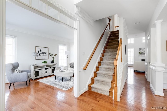 staircase with hardwood / wood-style flooring, crown molding, and decorative columns